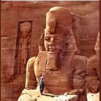A man stands on a colossal figure of Ramesses II at the temple of Abu Simbel in Egypt.